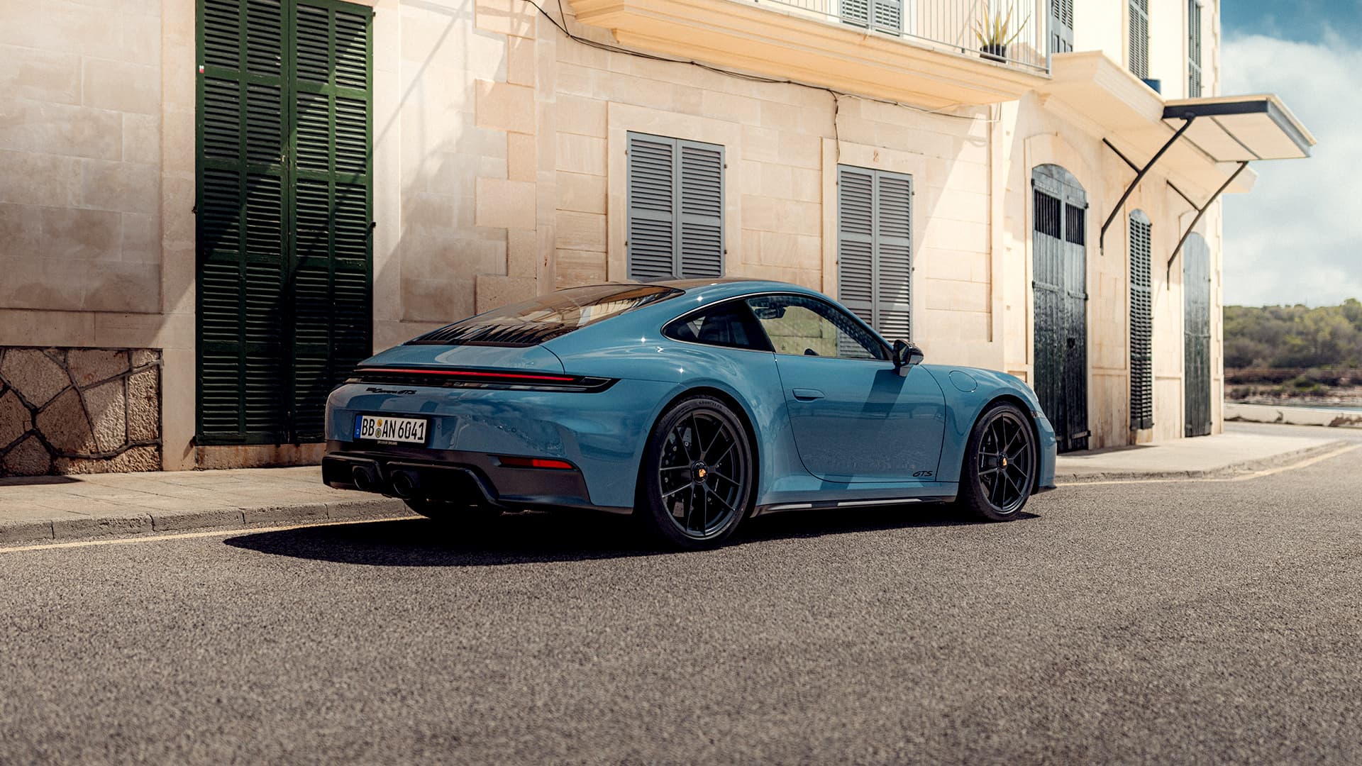 Blue Porsche 911 GTS parked beside a stone building
